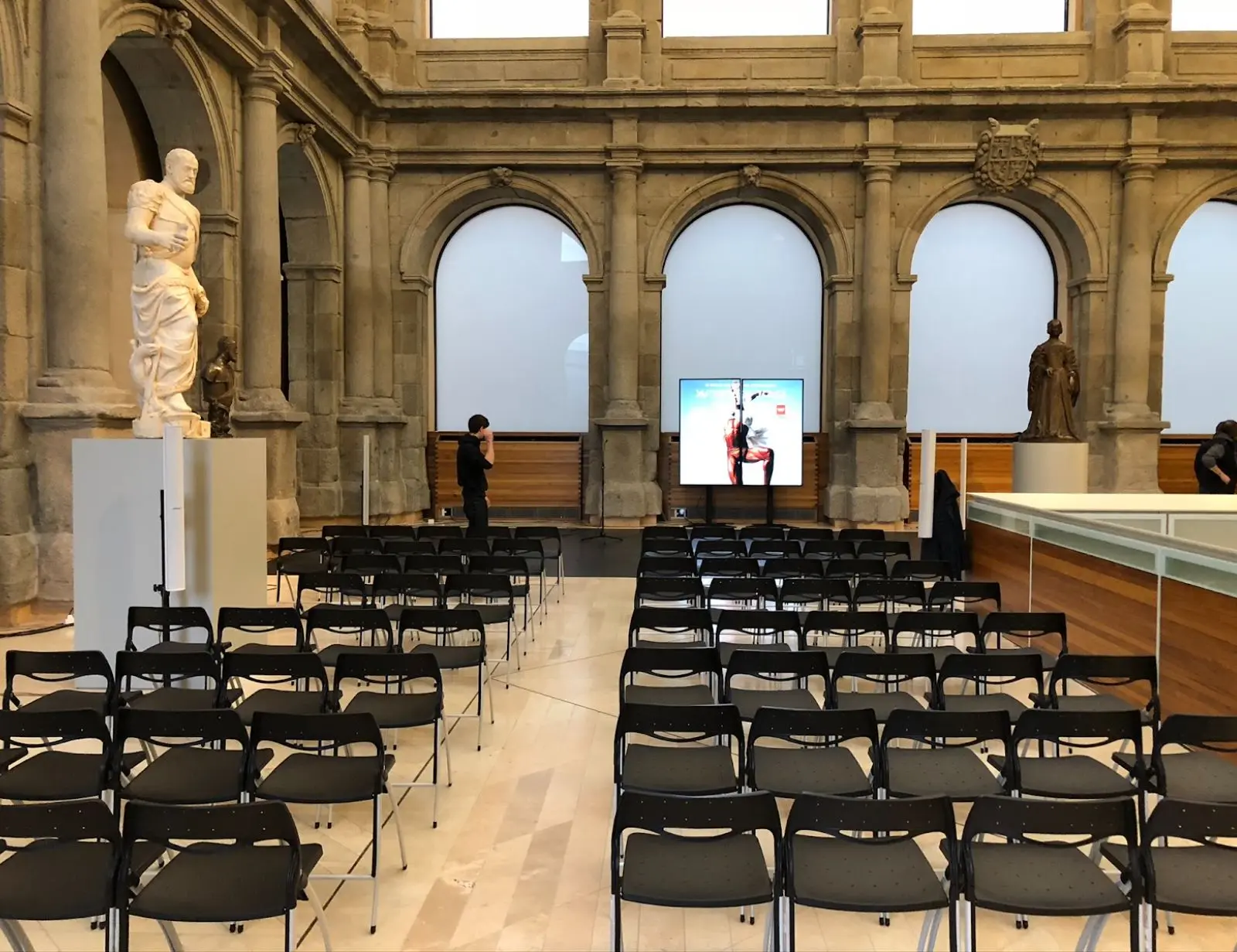 Sala con sillas vacías y estatuas clásicas.