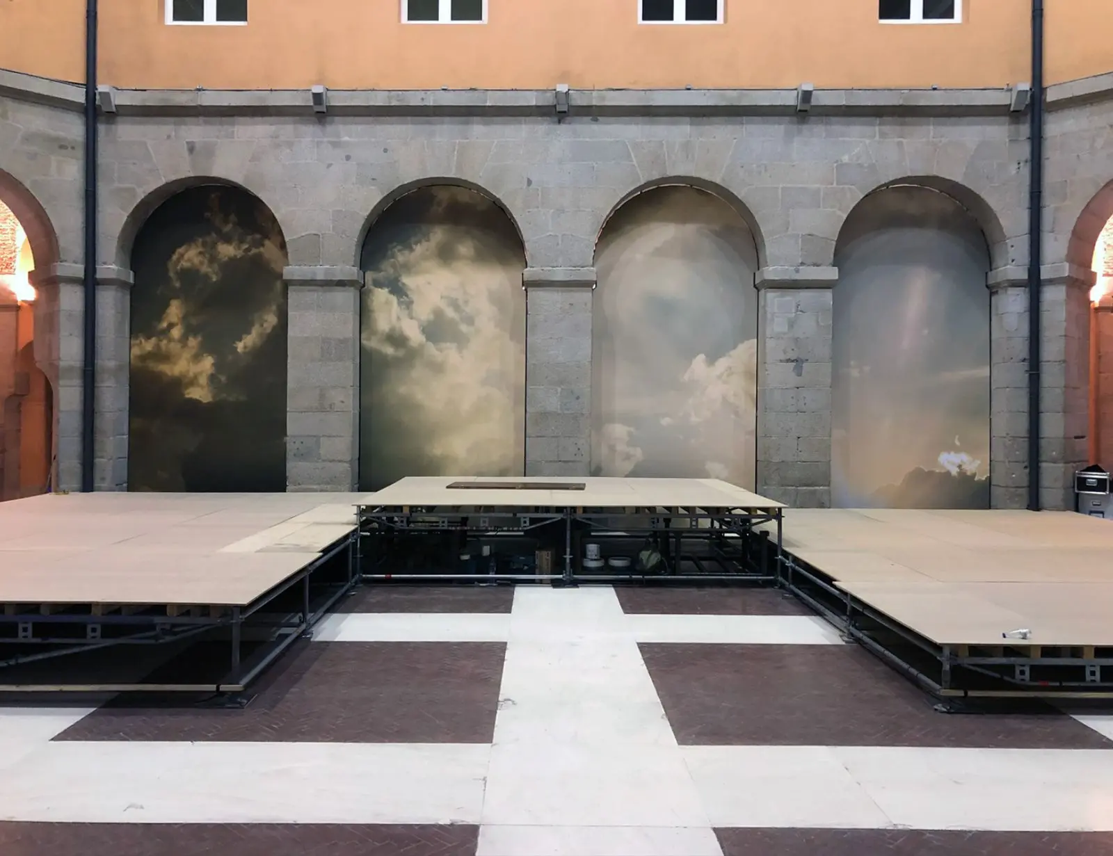 Escenario frente a murales de nubes en patio.